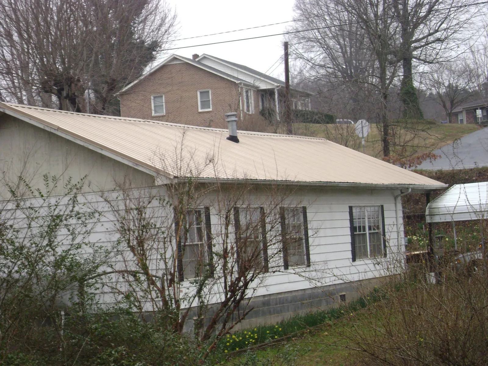 Tan metal roof on a white sided house set into a hillside — Commercial Roofing by Roofing Brothers in Montvale